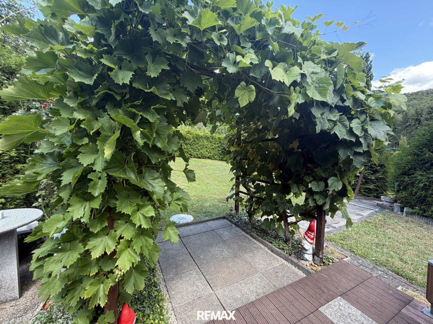 Grüner Gartenweg unter einem bewachsenen Torbogen, der zum Rasen führt.