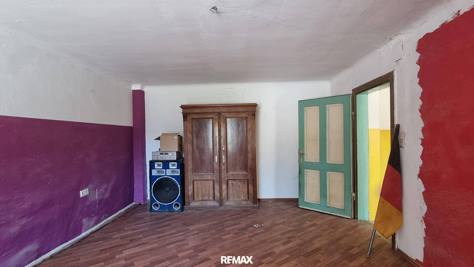 Geräumiger Raum mit Holzboden, farbigen Wänden und einem großen Holzschrank.