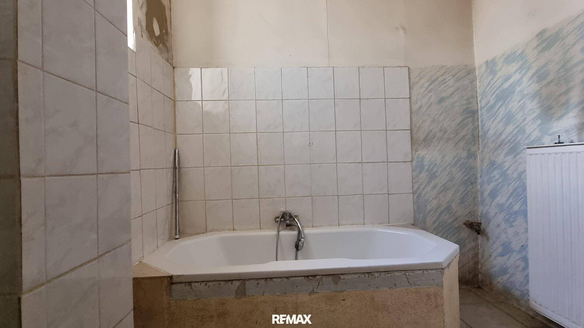 Badezimmer mit Eckbadewanne und Fliesen, das auf eine Renovierung wartet.