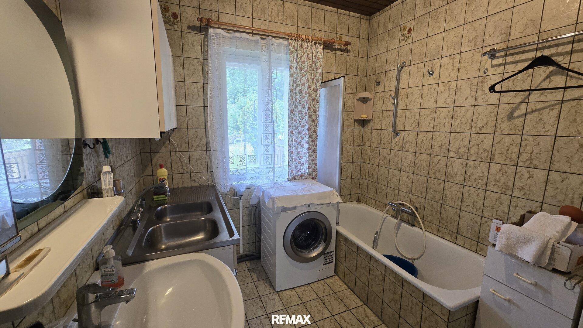Badezimmer mit Badewanne, Waschbecken, Waschmaschine und gefliesten Wänden.