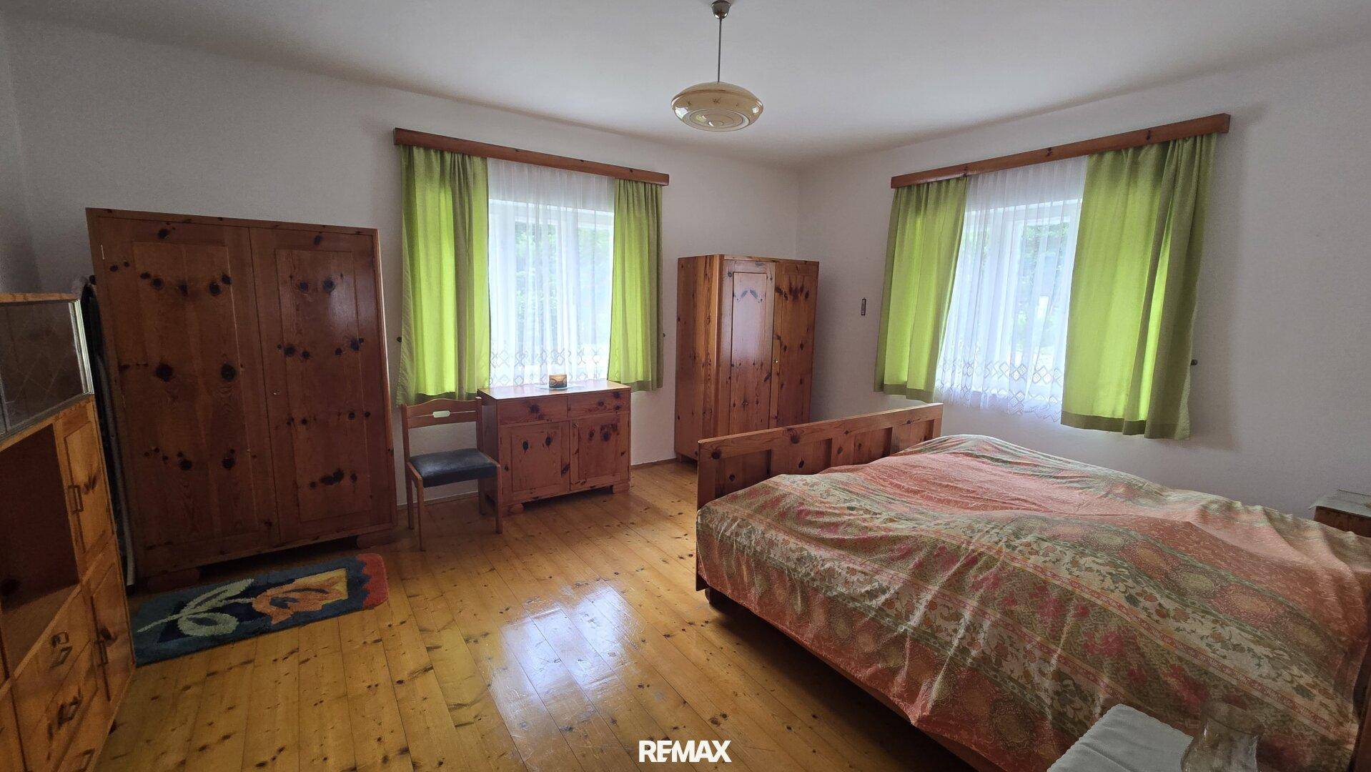 Helles Schlafzimmer mit Holzboden, zwei Fenstern und traditionellen Holzmöbeln.