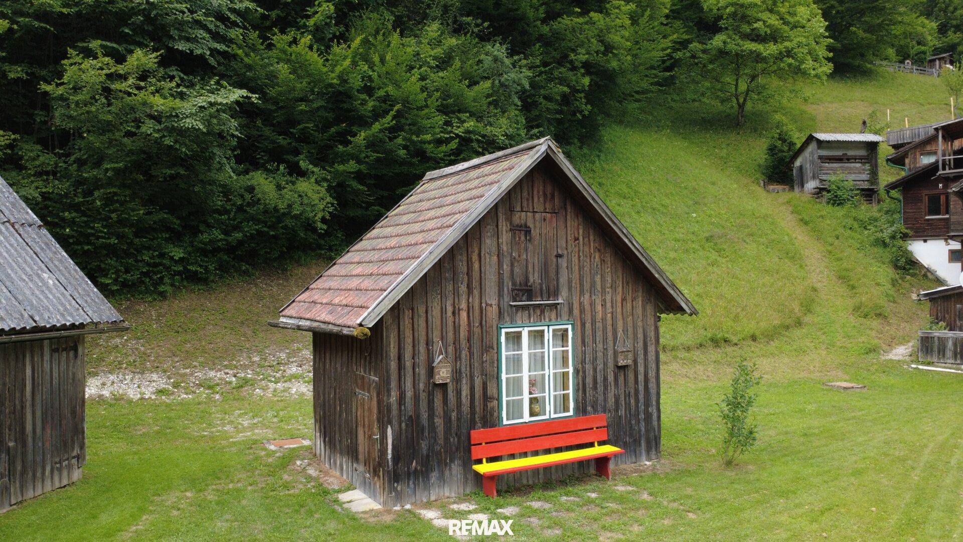 Kleines Holzschuppen mit roter und gelber Bank im Gartenbereich.
