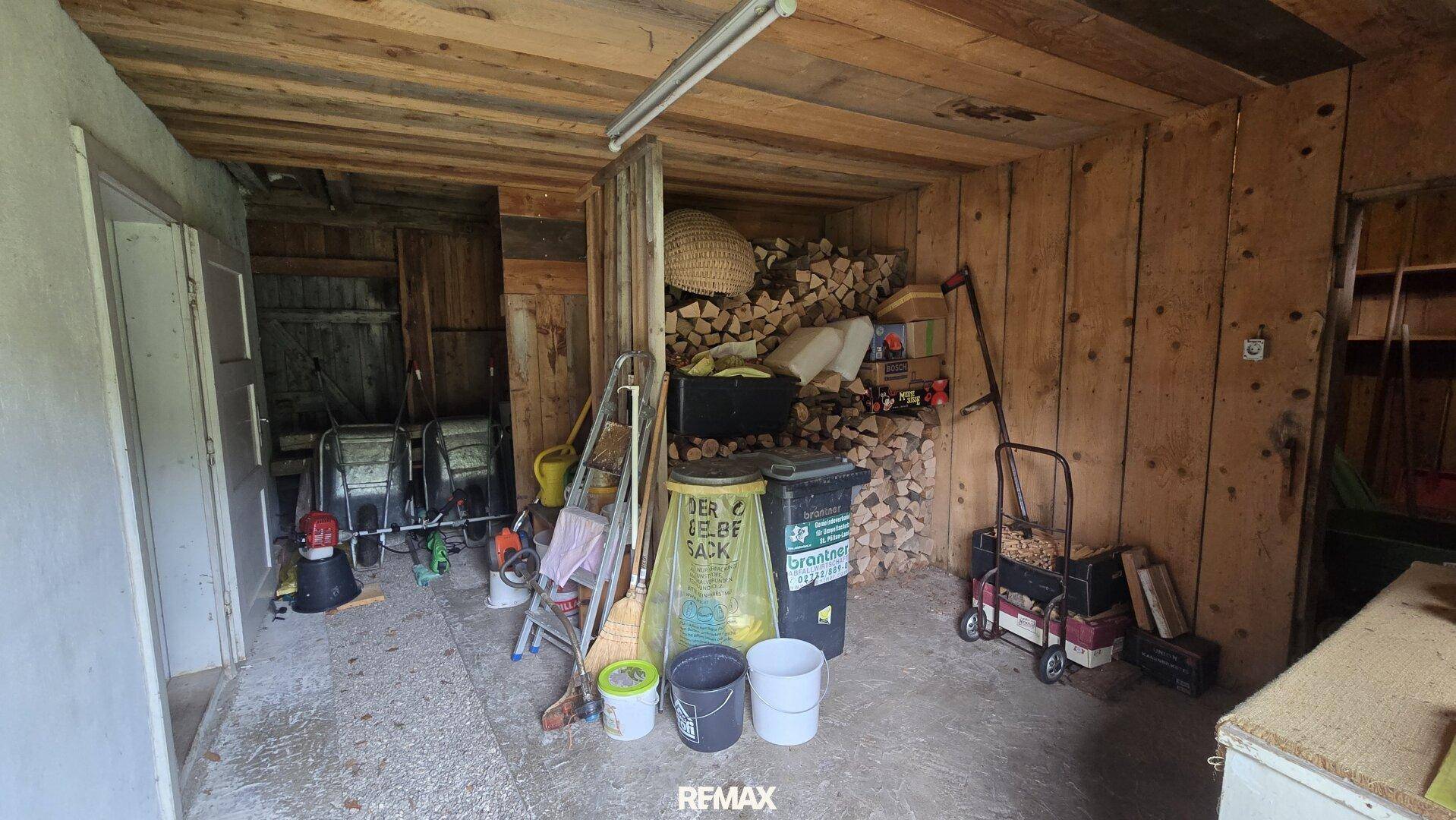 Abstellraum mit Holzstapeln, Werkzeugen und einfacher Holzverkleidung.