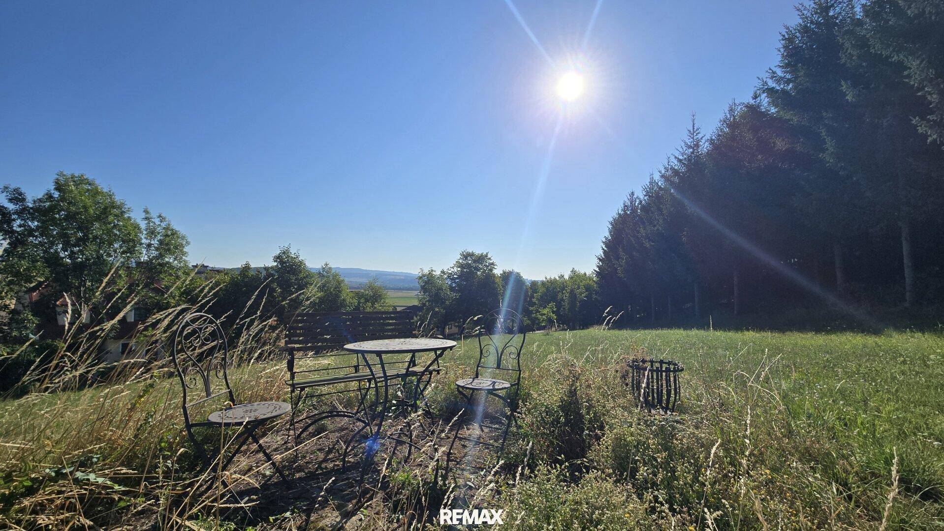 Gemütlicher Sitzbereich im Freien mit Metallmöbeln auf einer sonnigen Wiese, umgeben von Natur.