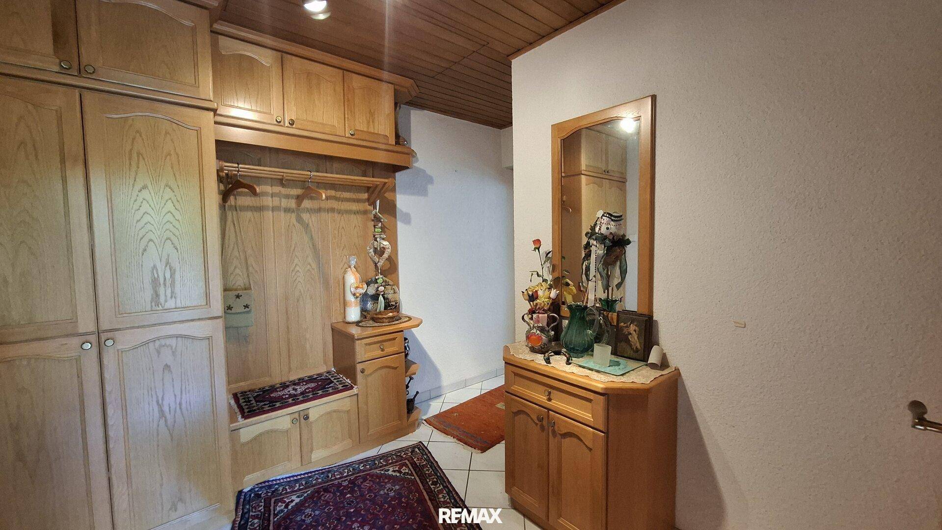 Eingangsbereich mit hellen Holzschränken, Garderobe und einem großen Spiegel.