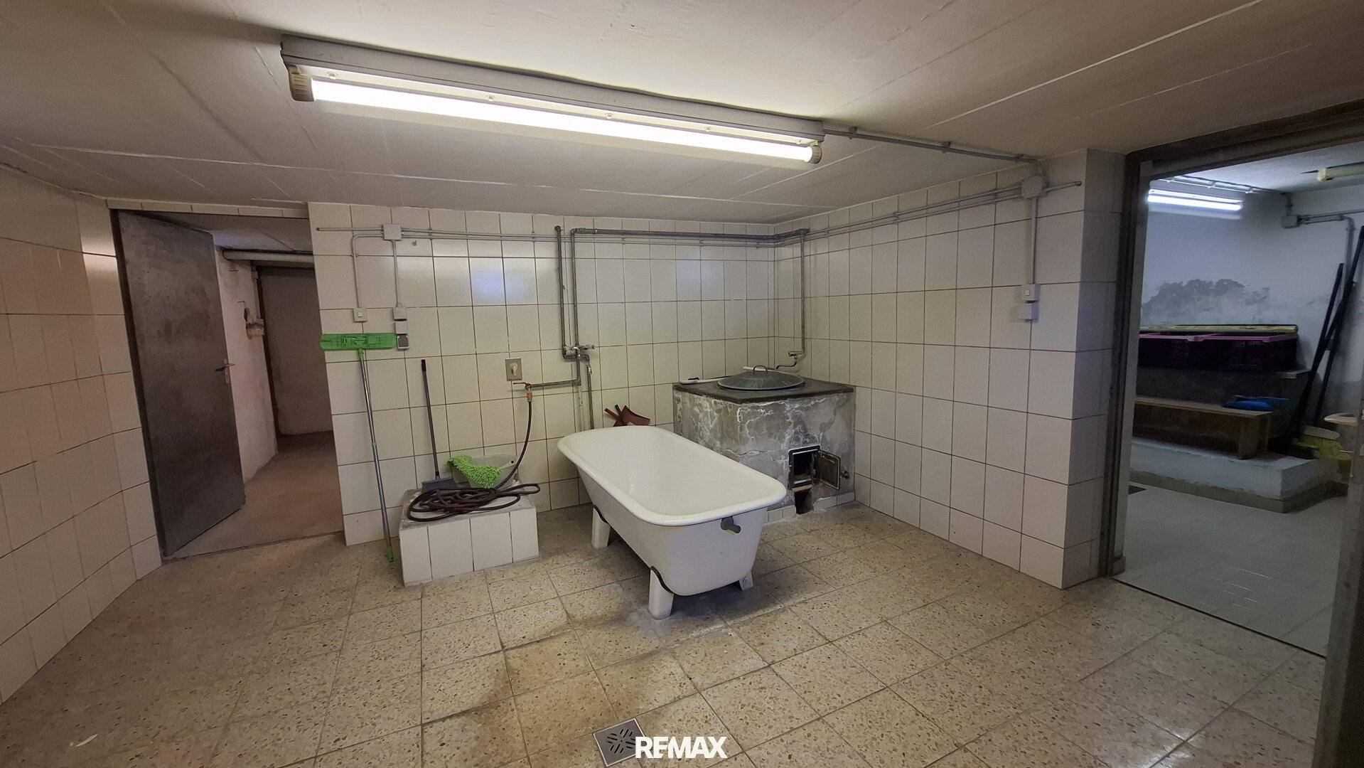 Kellerraum mit einer freistehenden Badewanne und gefliesten Wänden, möglicherweise als Waschküche genutzt.
