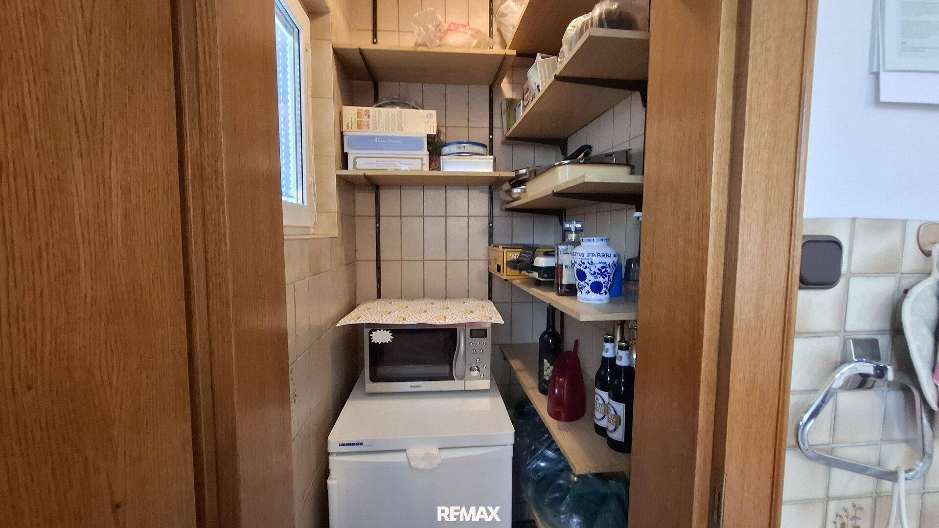 Praktische Speisekammer mit Regalen, Mikrowelle und kleinem Kühlschrank für zusätzlichen Stauraum.
