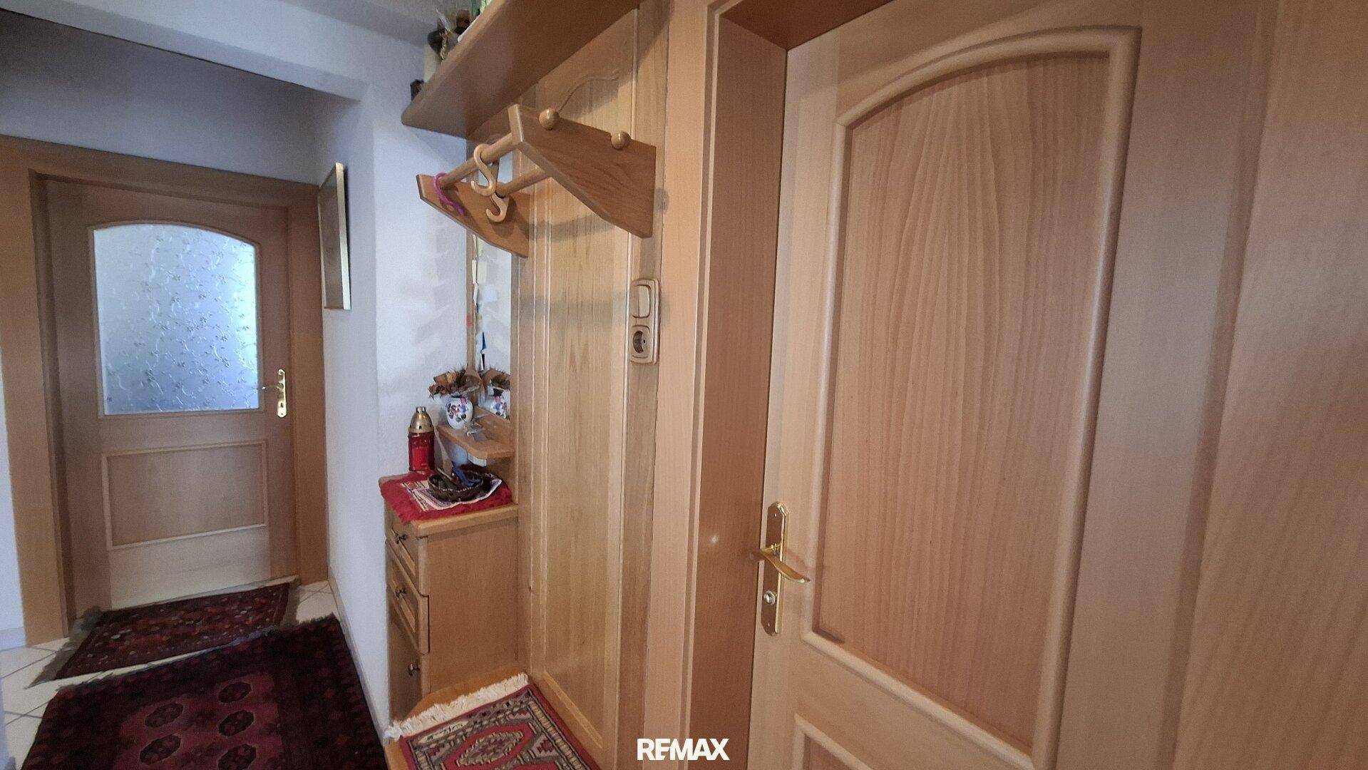 Heller Flur mit Holztüren, Garderobe und Teppichen auf dem Fliesenboden.