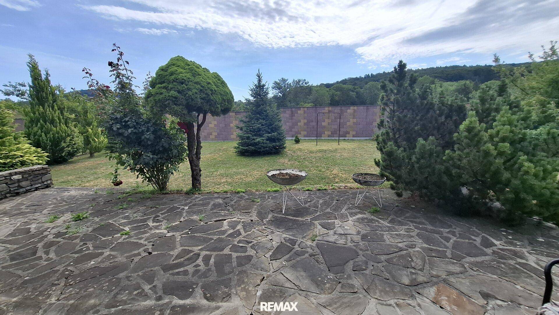 Großer Garten mit Steinterrasse, Rasenfläche und zwei Grillmöglichkeiten.