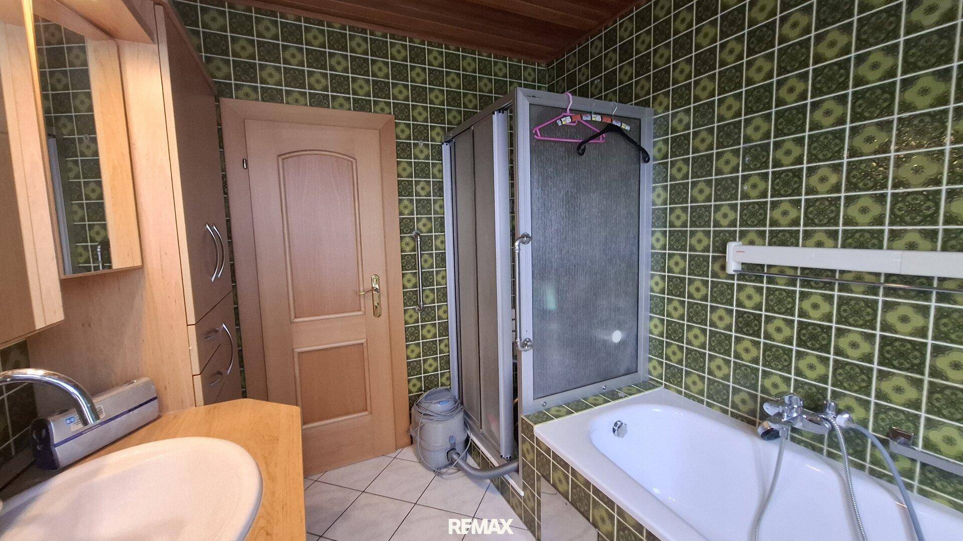 Badezimmer mit auffälligen grünen Fliesen, Badewanne und einer einfachen Duschkabine.