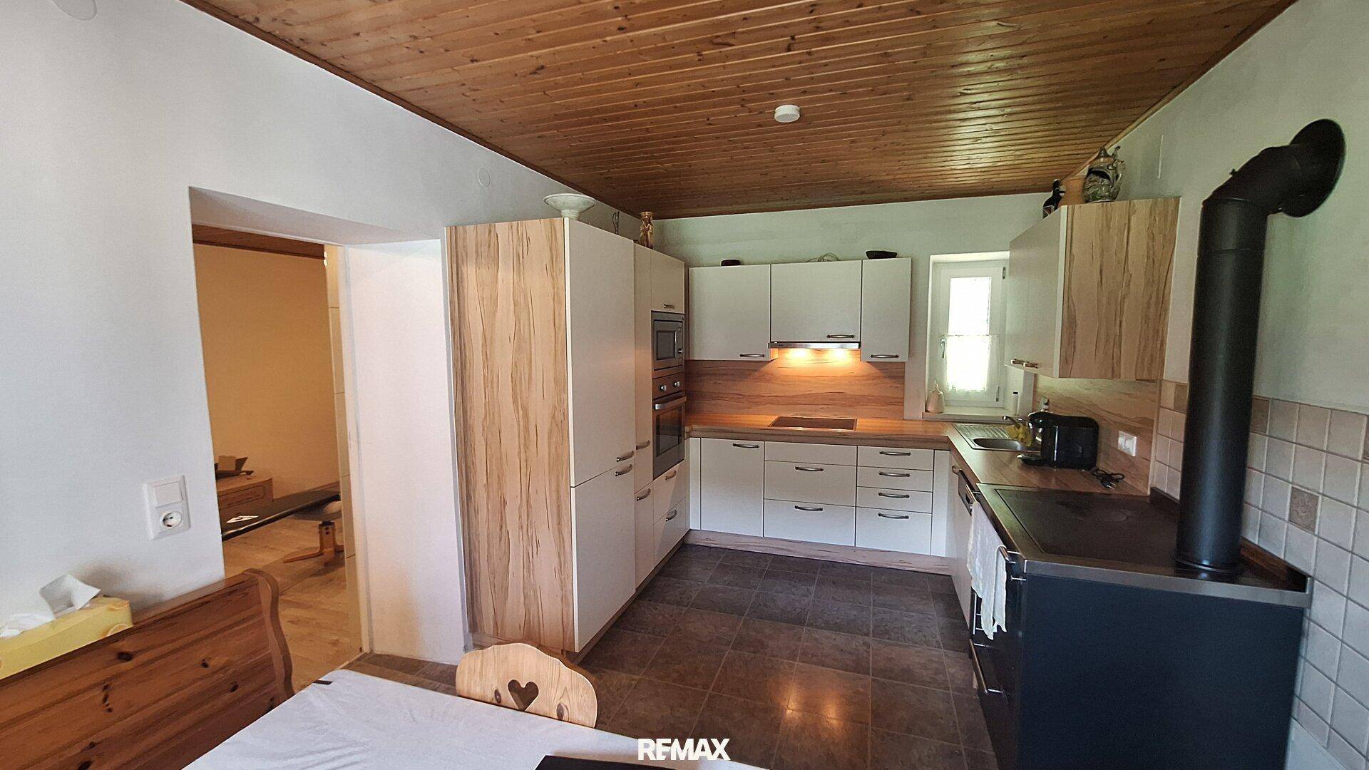 Gemütliche Küche mit Holzdecke, modernen Einbauschränken und einem traditionellen Holzofen.