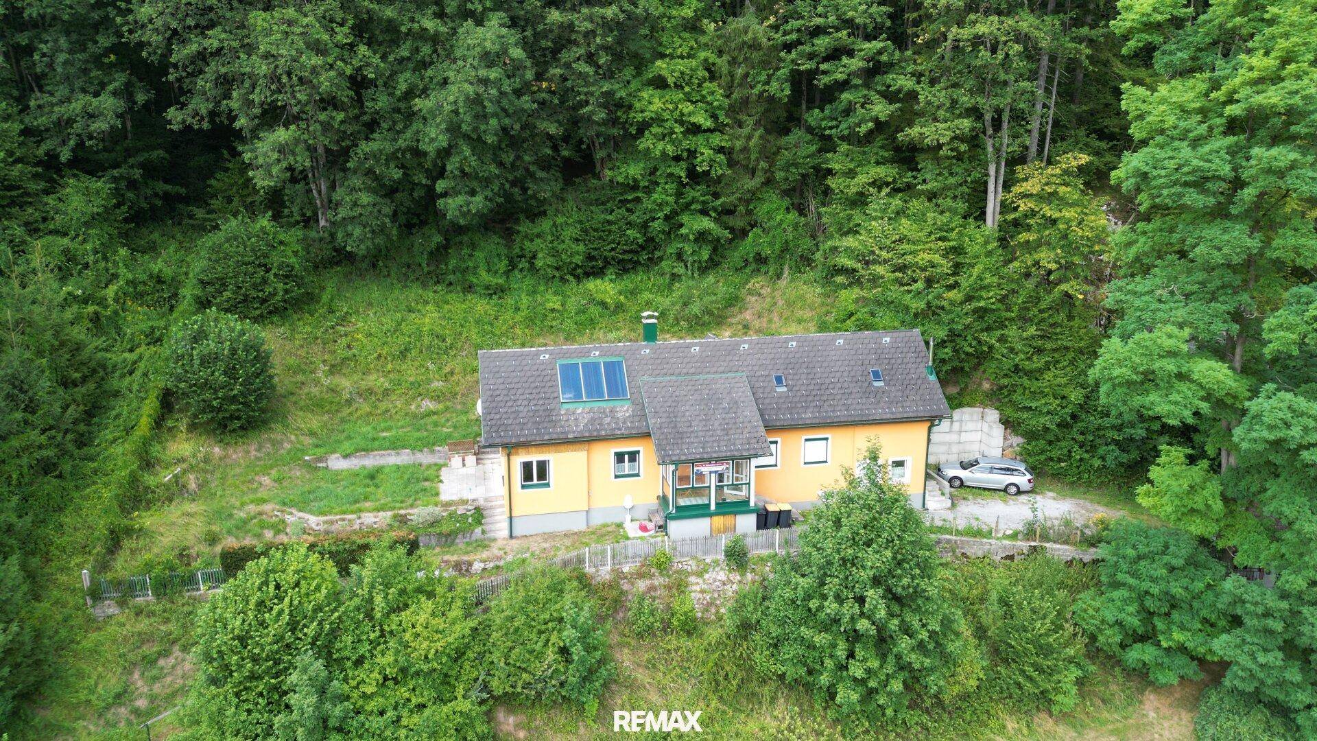 Freistehendes Haus mit Solarpaneelen auf dem Dach, umgeben von Wald und Wiesen in ländlicher Umgebung.