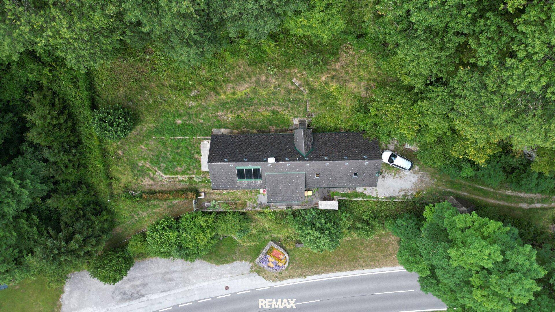 Vogelperspektive des Hauses, eingebettet in eine weitläufige grüne Landschaft mit angrenzender Straße.