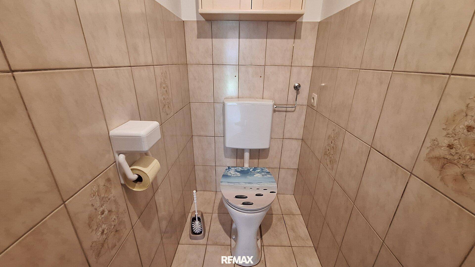 Separate Toilette mit beigefarbenen Fliesen an Wänden und Boden.