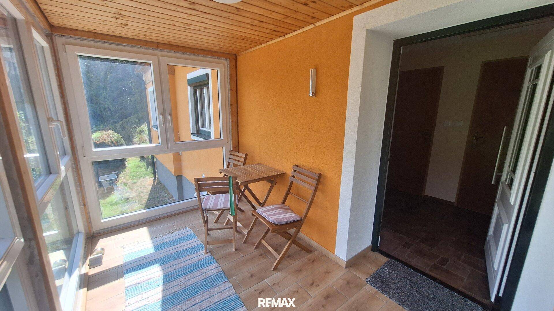 Heller Wintergarten mit Holzdecke und Blick ins Grüne, ausgestattet mit einem kleinen Tisch und Stühlen.