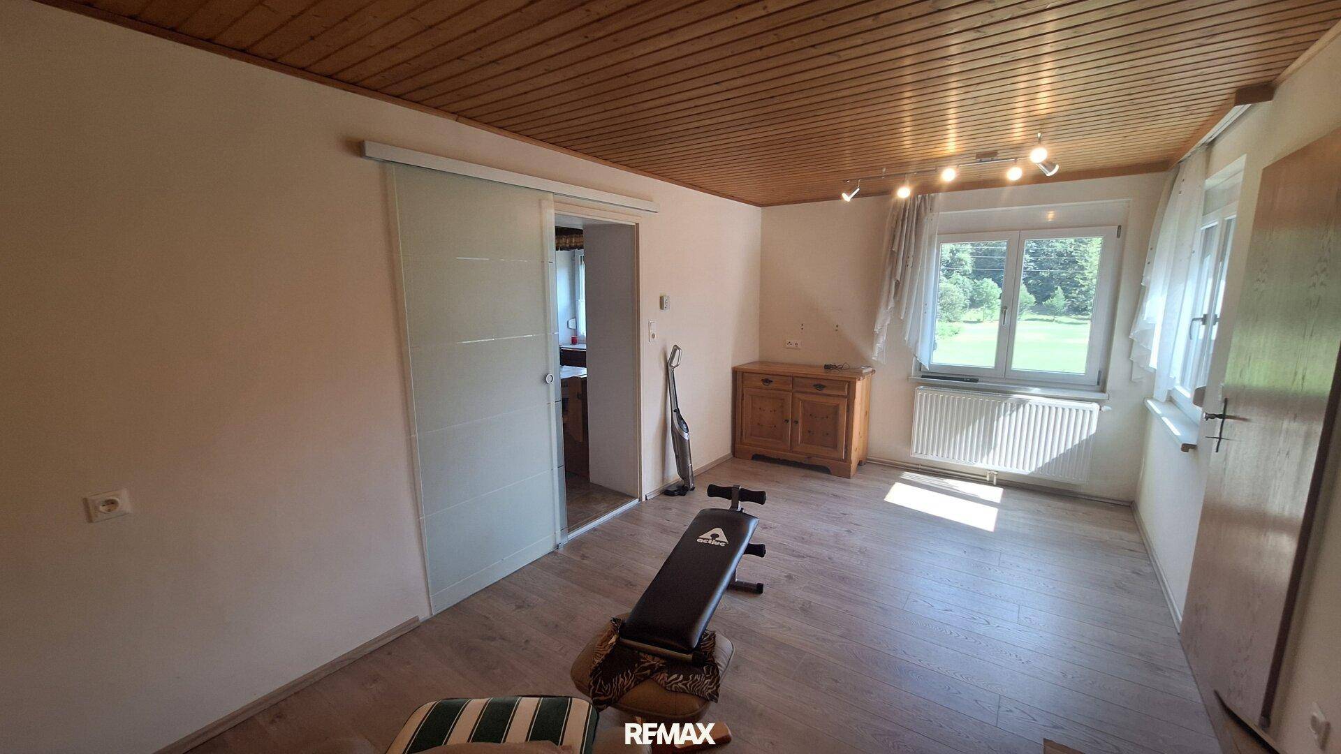 Heller Raum mit Holzdecke, Laminatboden und einem Fenster mit Blick ins Grüne.