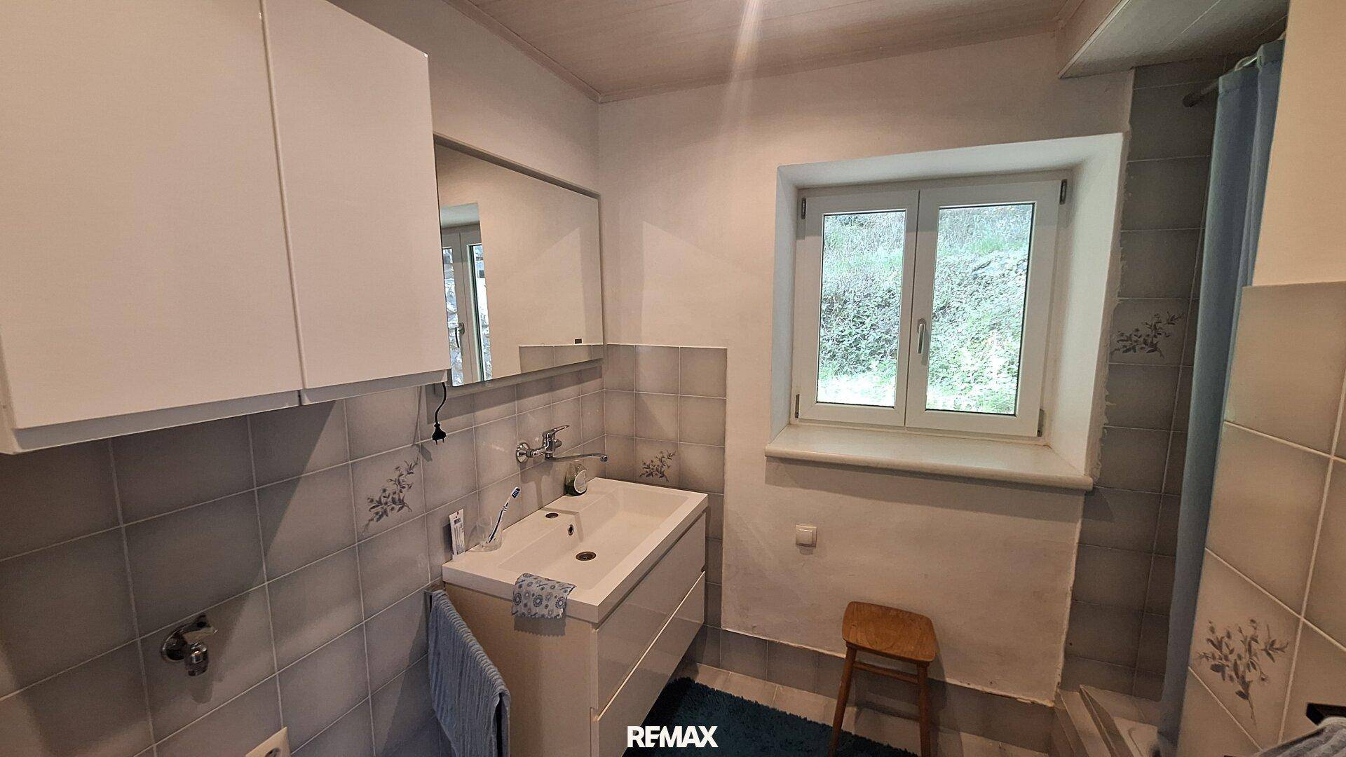 Badezimmer mit Waschbecken, Spiegelschrank und einem Fenster, das Tageslicht hereinlässt.