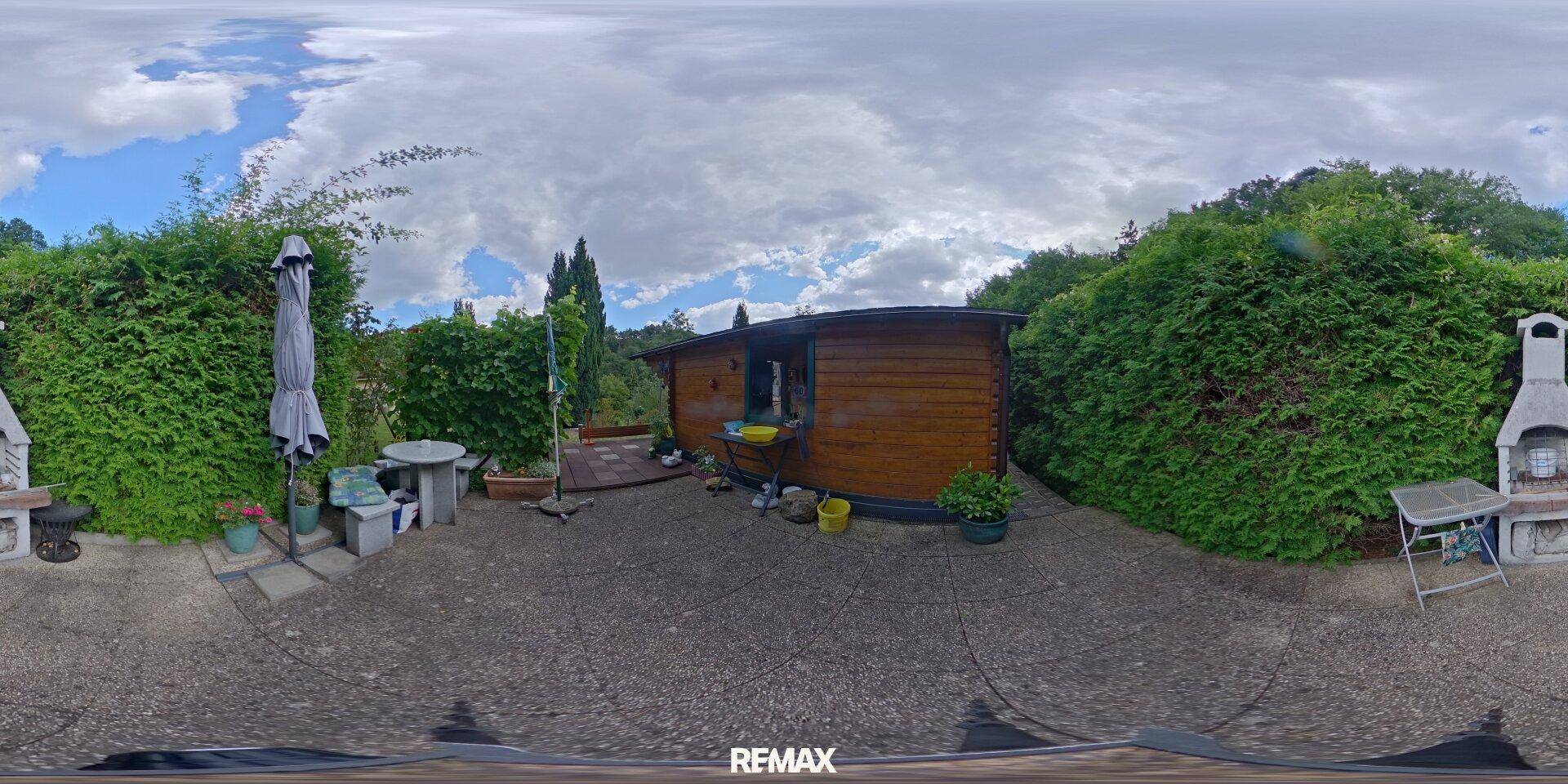 Gepflasterter Außenbereich mit Grillplatz und Sitzgelegenheiten vor dem Holzhaus.