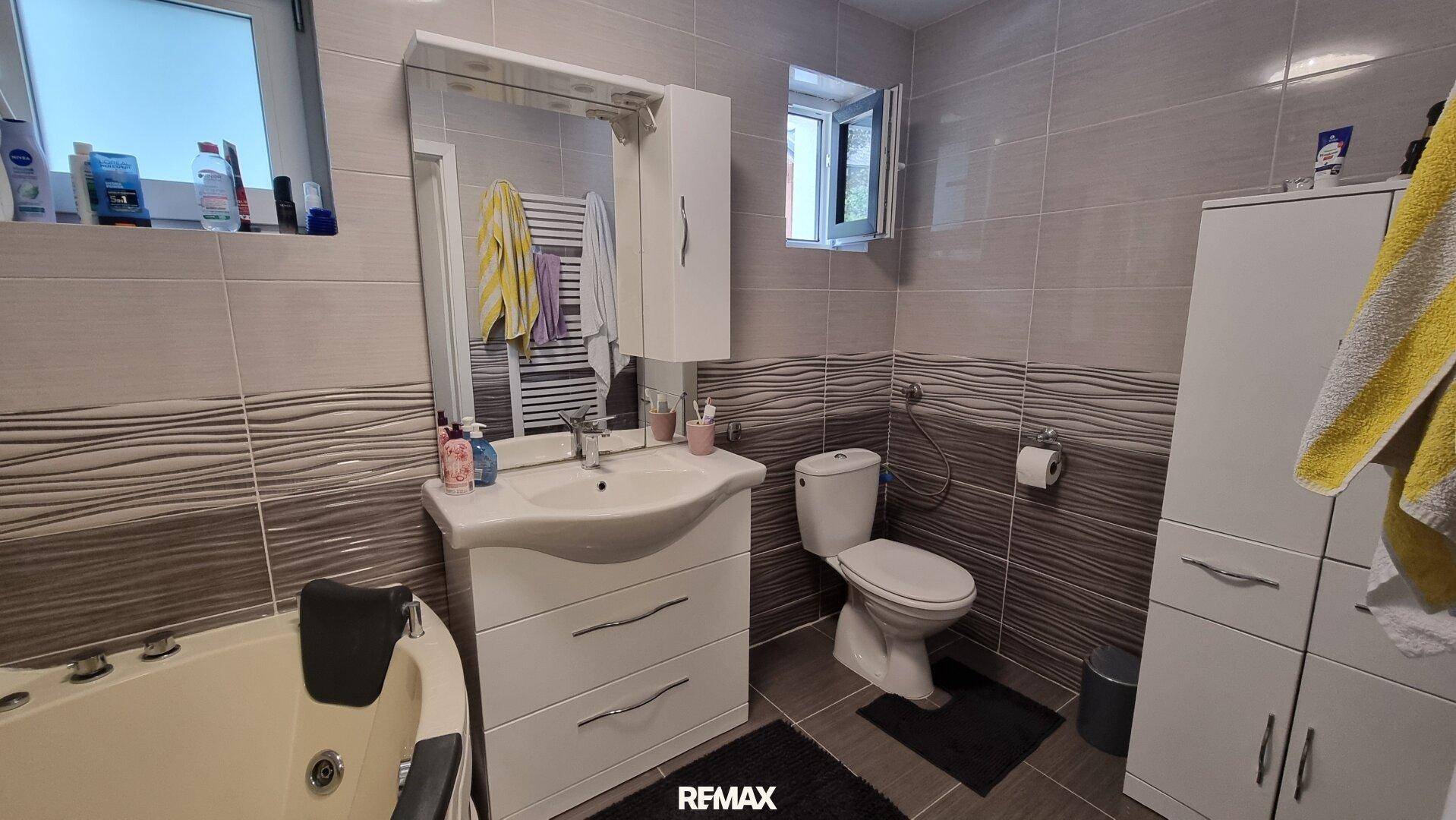 Geräumiges Badezimmer mit Eckbadewanne, WC, Waschtisch und Spiegelschrank, hell gefliest.