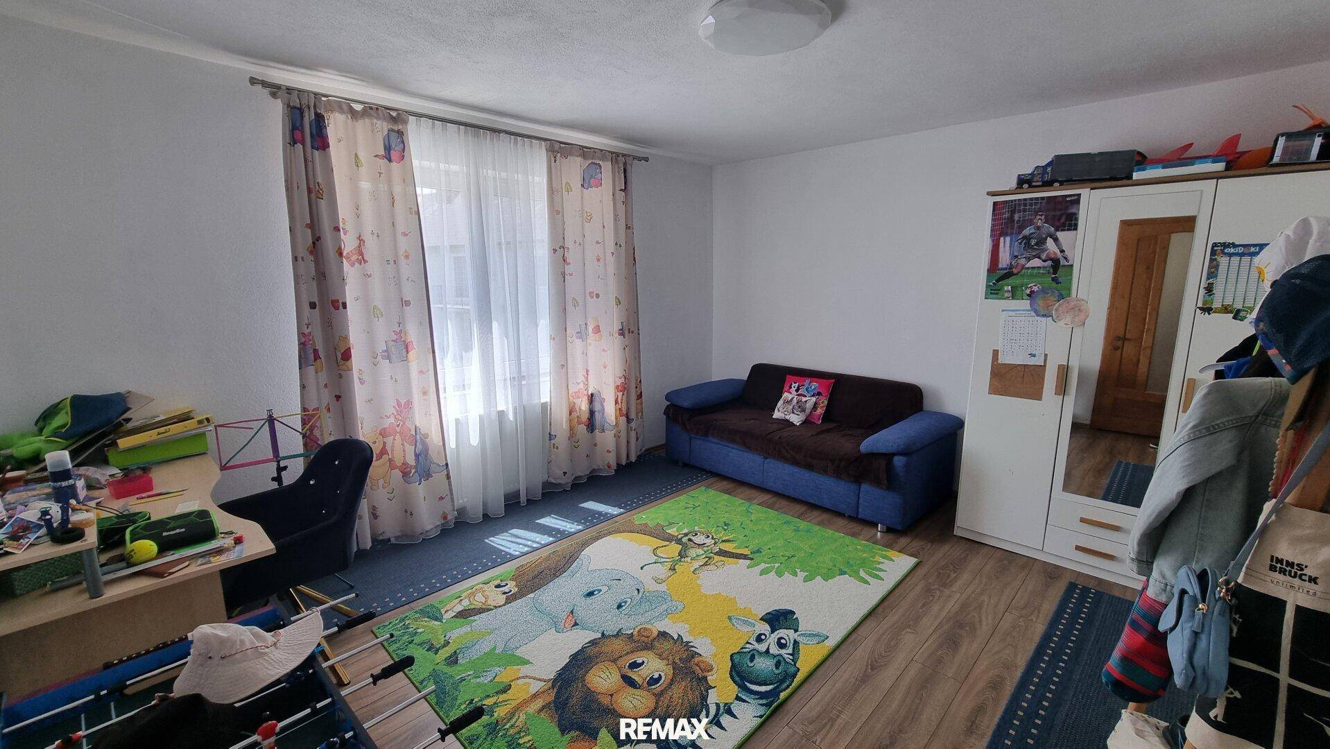 Kinderzimmer mit blauem Sofa, weißem Kleiderschrank, Schreibtisch und farbenfrohem Teppich.