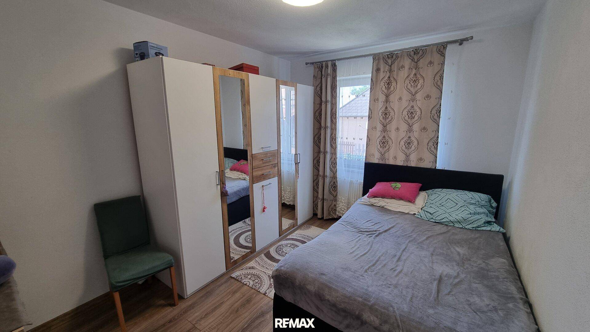 Schlafzimmer mit Einzelbett, großem Kleiderschrank mit Spiegeltüren und Fenster mit Vorhängen.