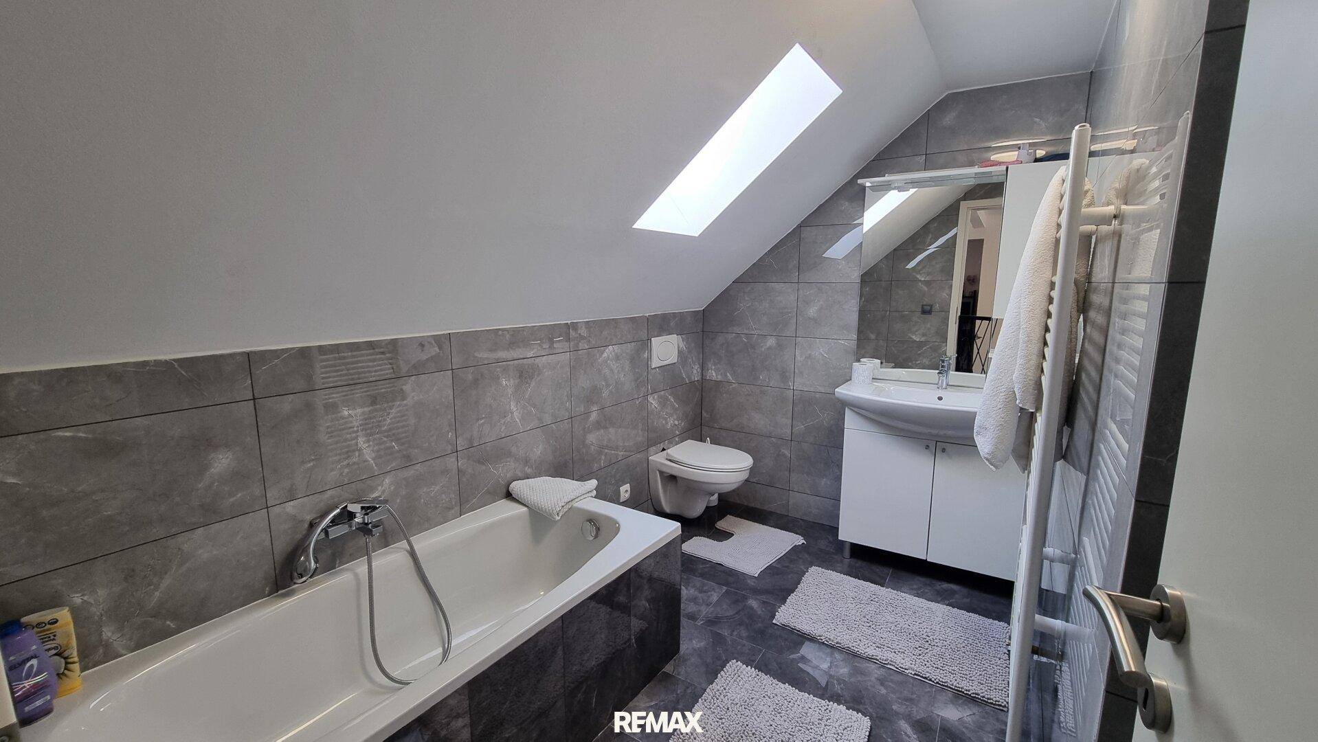 Modernes Badezimmer im Dachgeschoss mit Badewanne, WC, Waschtisch, Handtuchheizkörper und Dachfenster.