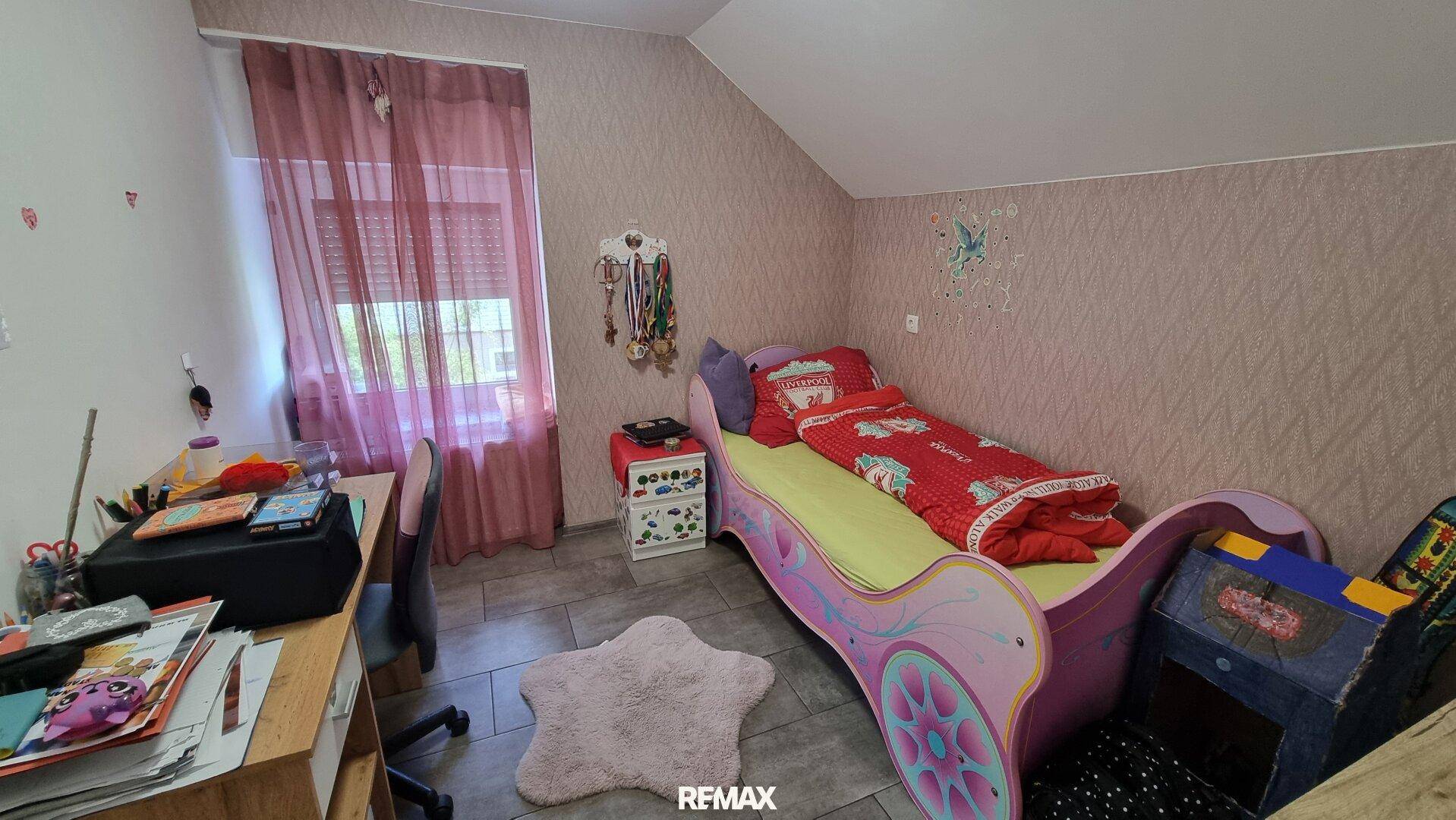 Helles Kinderzimmer mit rosa Bett, Schreibtisch und gemusterter Tapete, ideal für kleine Bewohner.