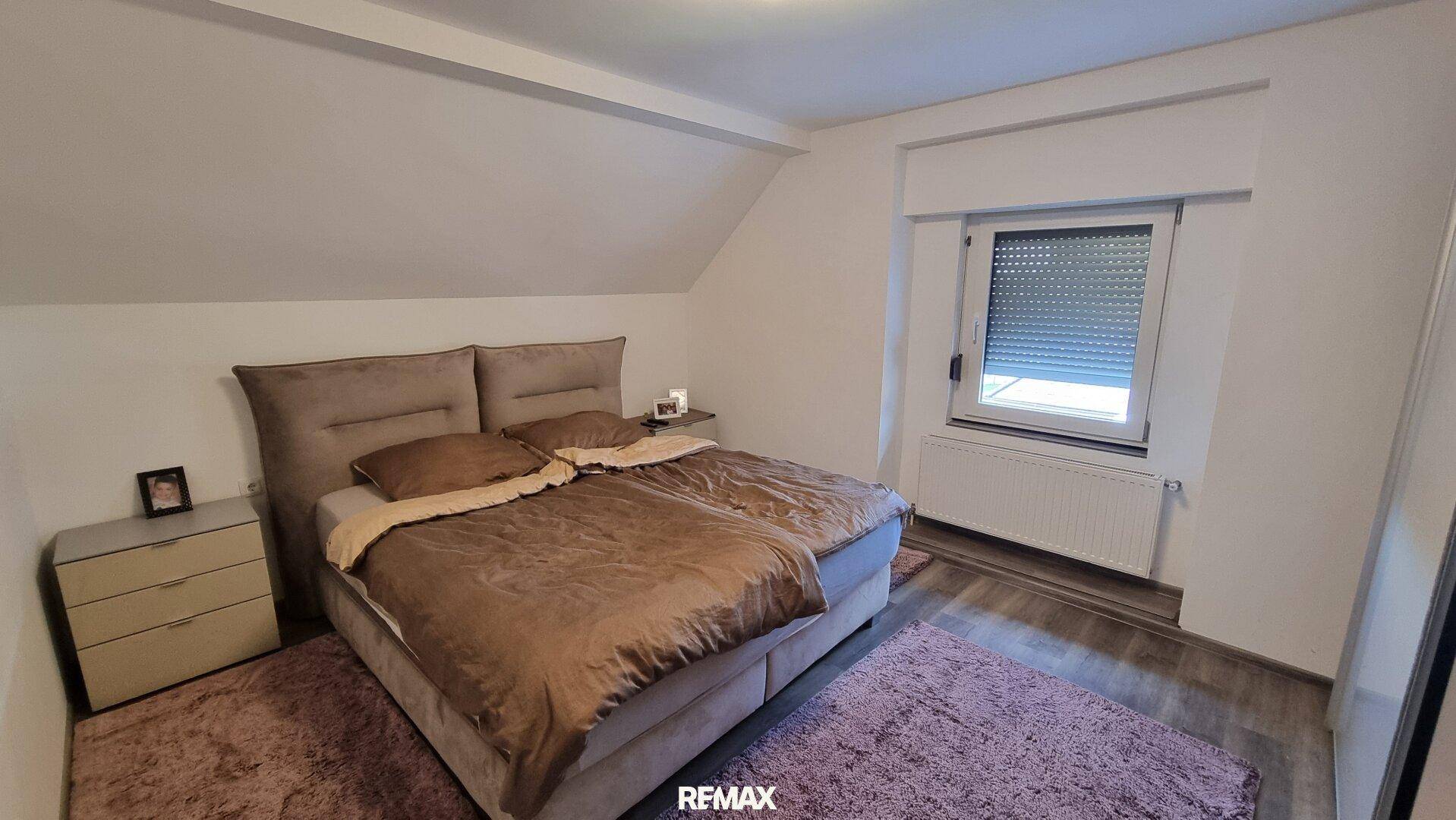 Schlafzimmer im Dachgeschoss mit Doppelbett, schrägen Decken und einem Fenster mit Rollladen.