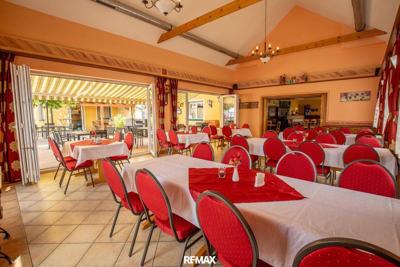 Großer Speisesaal mit roten Stühlen und Tischen, ideal für Veranstaltungen, mit Zugang zur Terrasse.