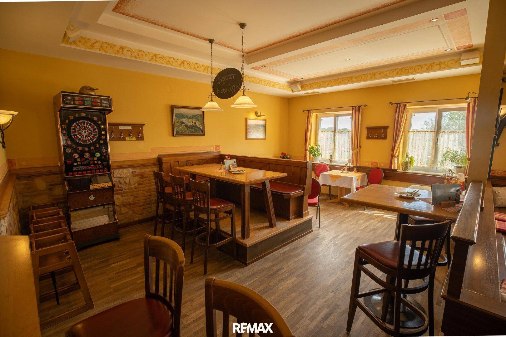 Gemütlicher Restaurantbereich mit erhöhten Sitzgelegenheiten und einem Dartspielautomaten.