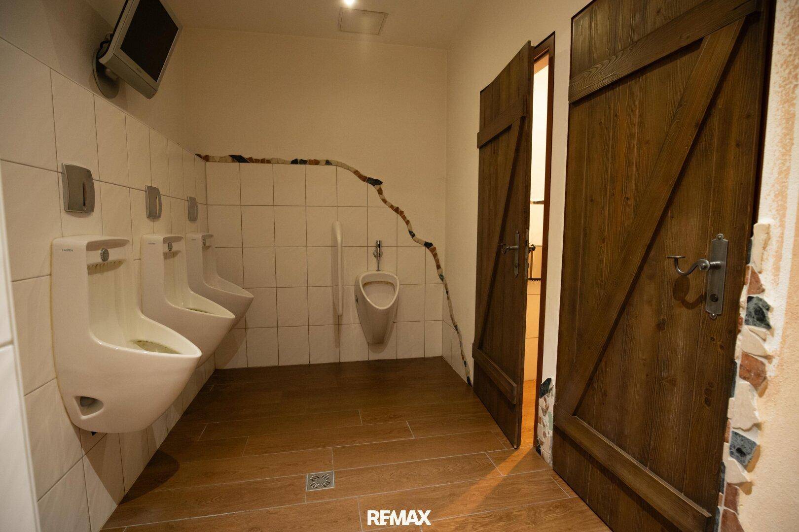 Herren-WC mit Urinalen und rustikalen Holztüren, die den traditionellen Stil fortsetzen.