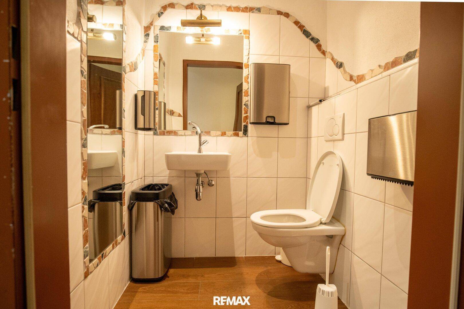 WC-Kabine mit Toilette, Waschbecken und Spiegel, ausgestattet mit hellen Fliesen.