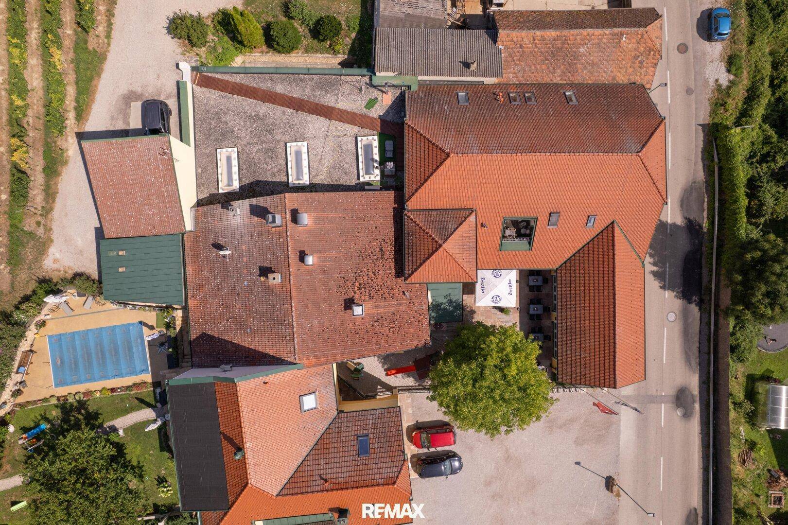 Draufsicht auf den Gebäudekomplex mit mehreren Dächern, einem Pool und Parkplätzen, umgeben von Grünflächen.