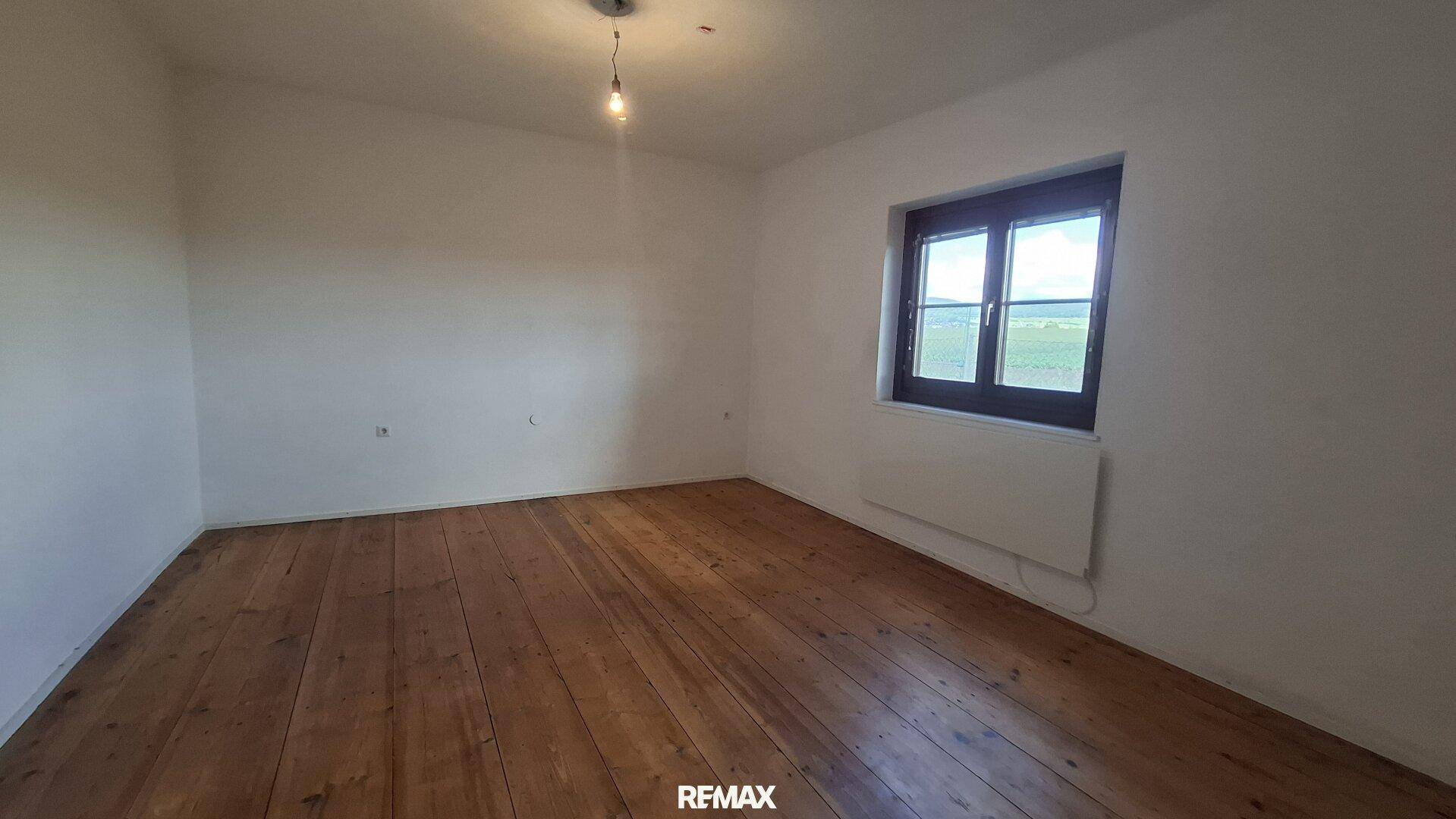 Helles Zimmer mit rustikalem Holzplankenboden und Blick ins Grüne.