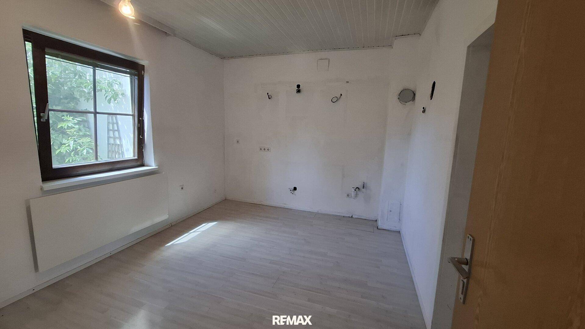Leerer Raum, vorbereitet für eine Küche, mit hellem Laminatboden und Fenster.