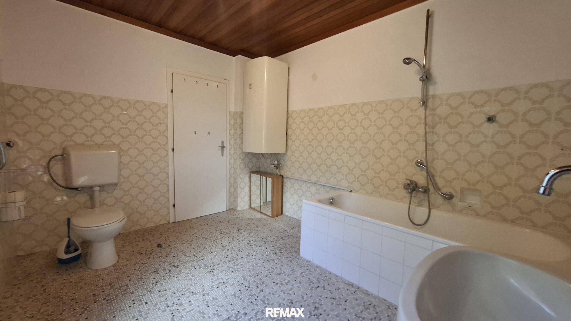 Badezimmer mit Badewanne, WC und gemusterten Wandfliesen im Retro-Stil.