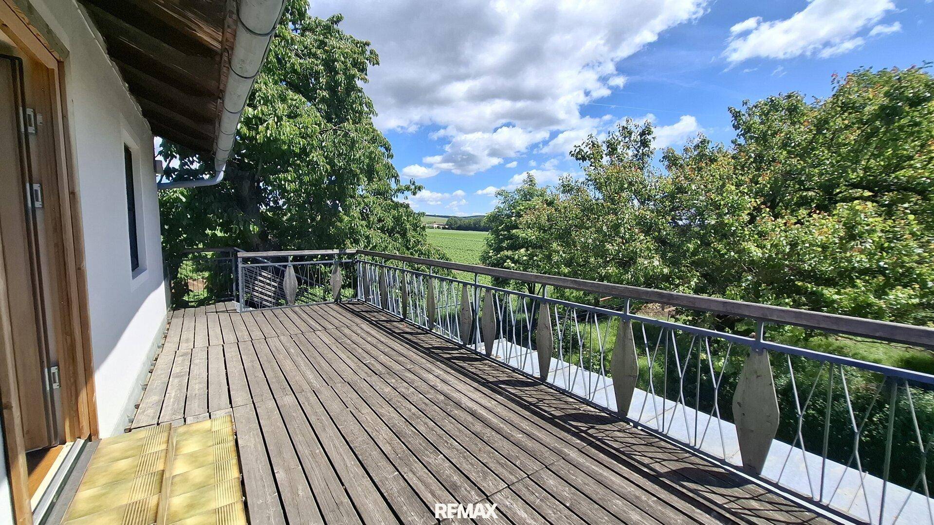 Großer Holzbalkon mit Metallgeländer und weitem Blick über die grüne Landschaft.