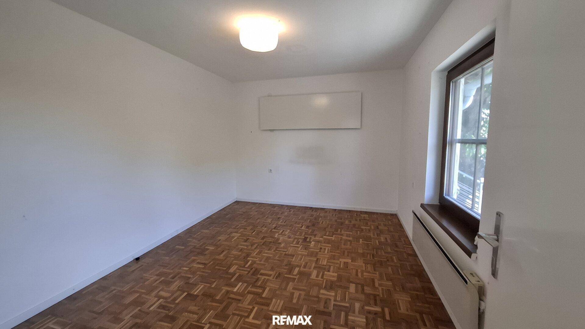 Helles Zimmer mit klassischem Parkettboden und Fenster.