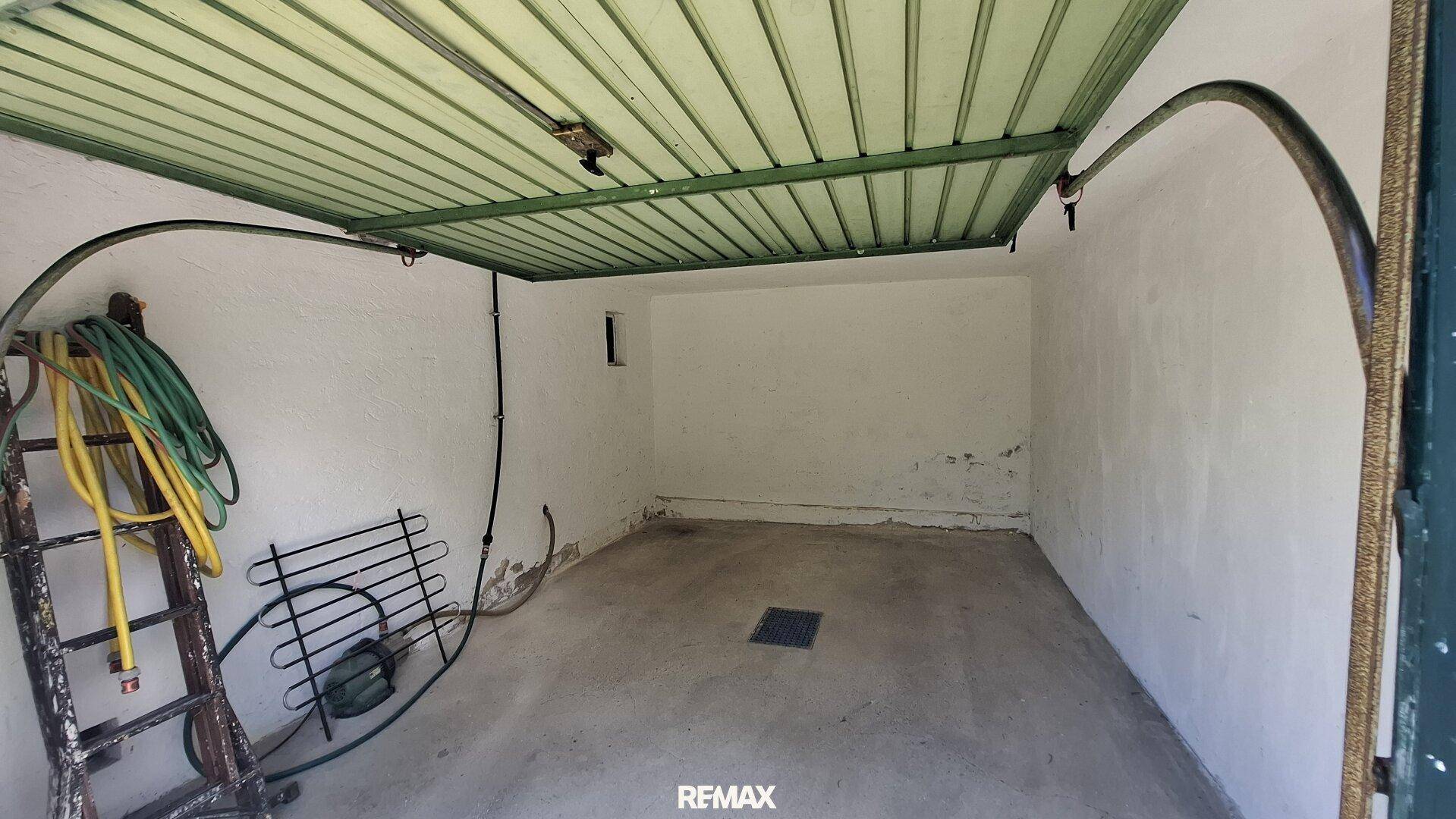 Leere Garage mit Betonboden und grünem Garagentor.