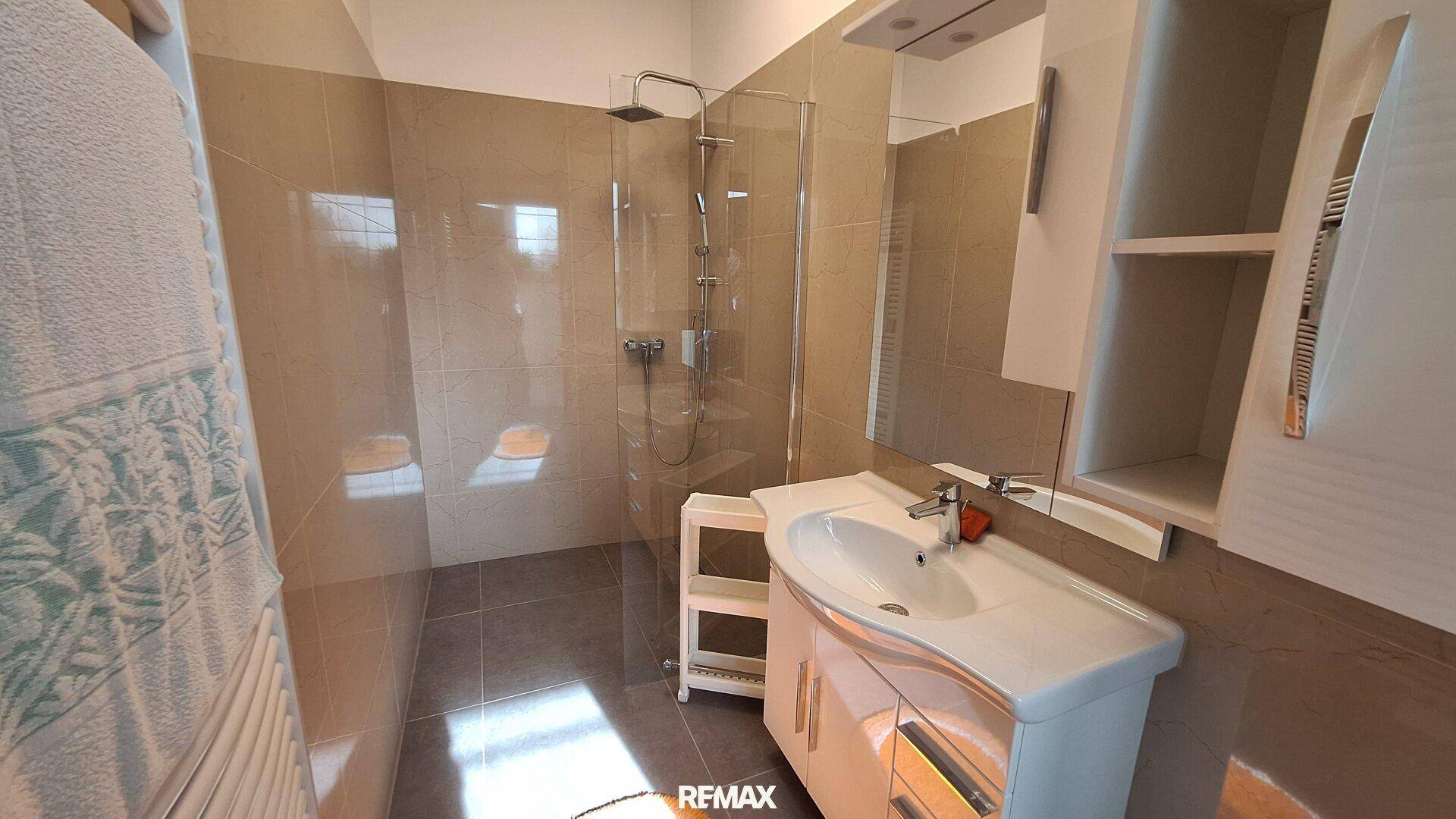Modernes Badezimmer mit beigefarbenen Fliesen, ebenerdiger Dusche und einem einzelnen Waschbecken.