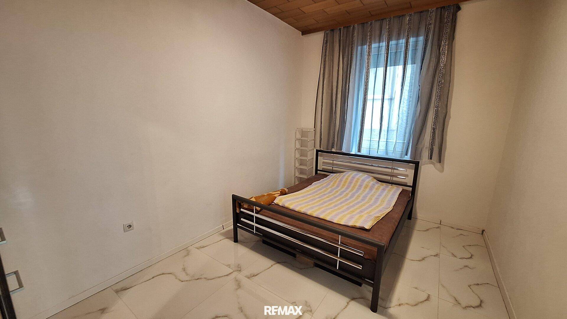 Kleines Schlafzimmer mit Fliesenboden, Einzelbett und einem Fenster mit Vorhängen.