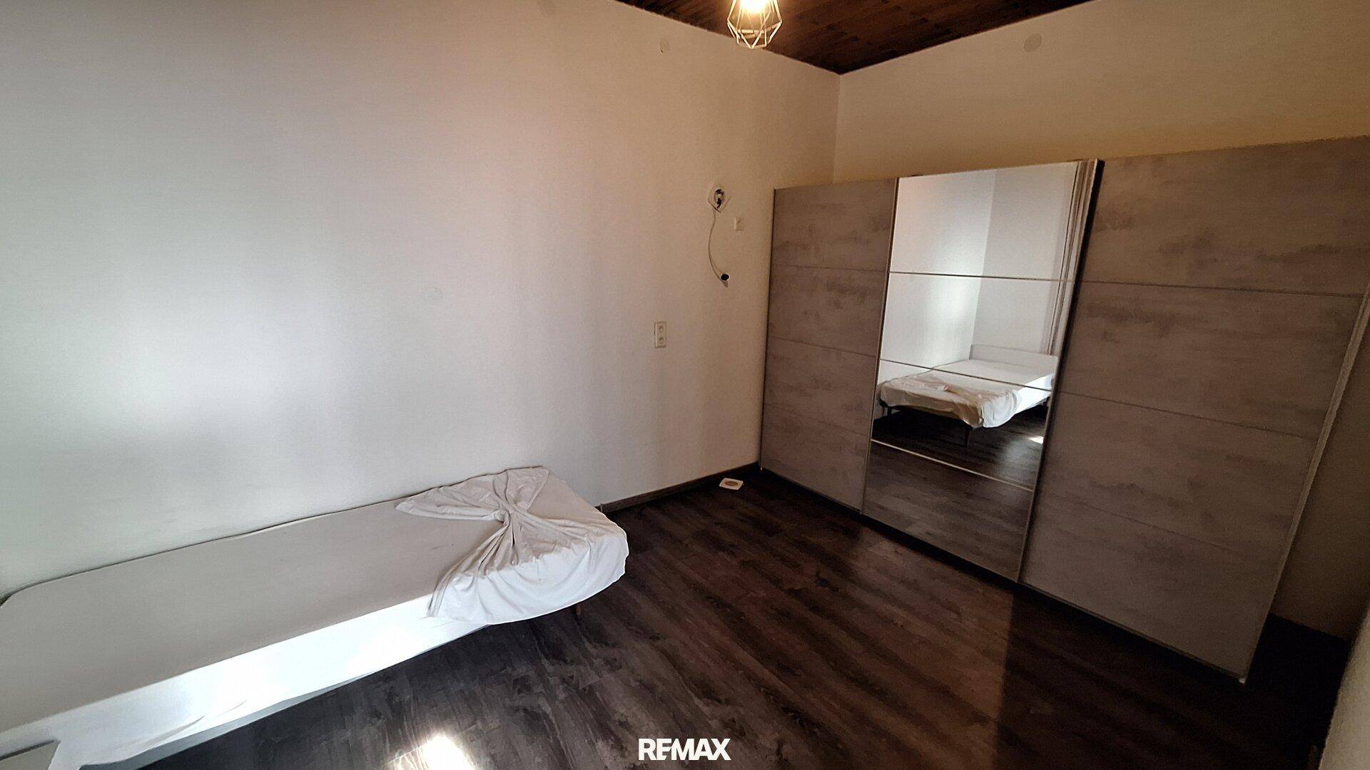 Schlafzimmer mit dunklem Laminatboden, Spiegelschrank und einem Einzelbett.
