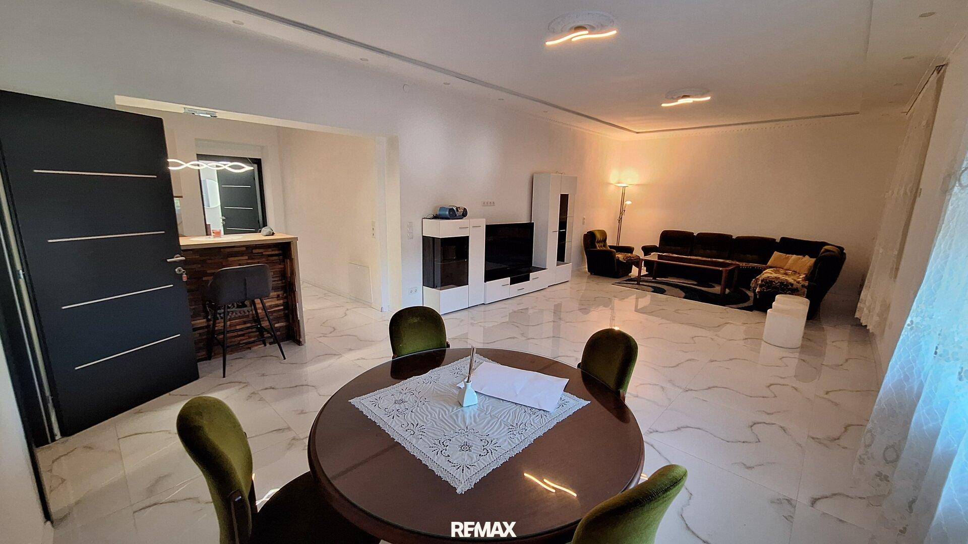 Geräumiger Wohn- und Essbereich mit modernen Fliesen, dunklem Sofa und einer Bar im Hintergrund.