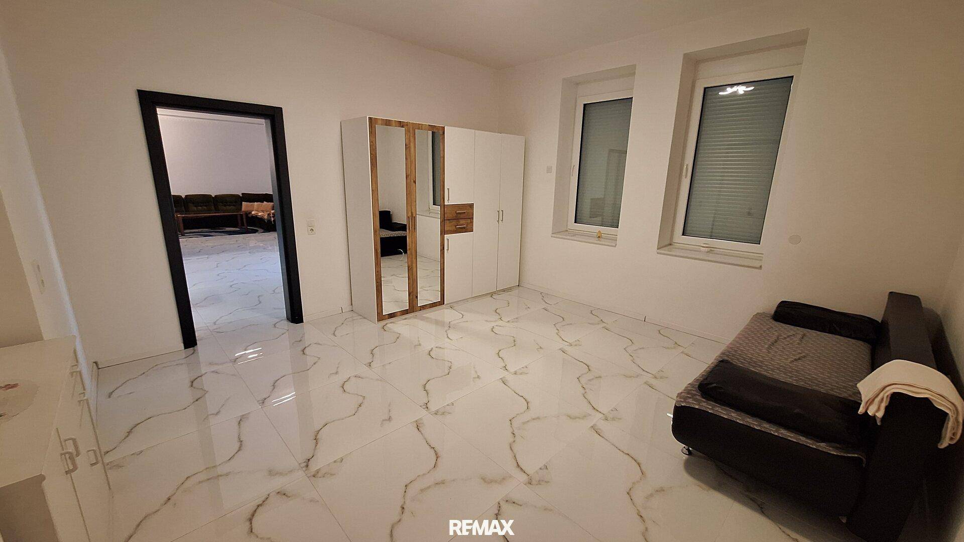 Geräumiges Schlafzimmer mit weißen Fliesen, großem Spiegelschrank und Blick auf den Wohnbereich.