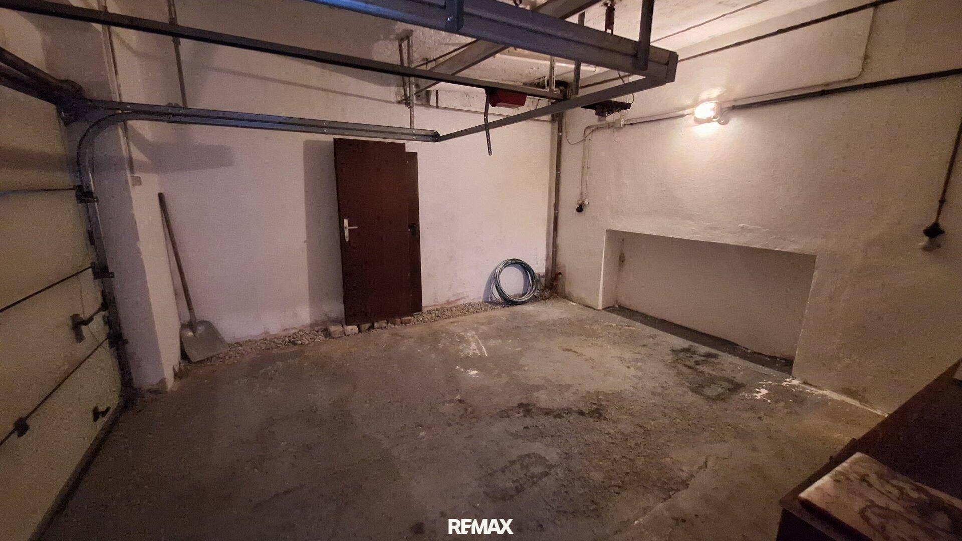 Geräumige Garage mit Betonboden, Garagentor und einer zusätzlichen Tür.