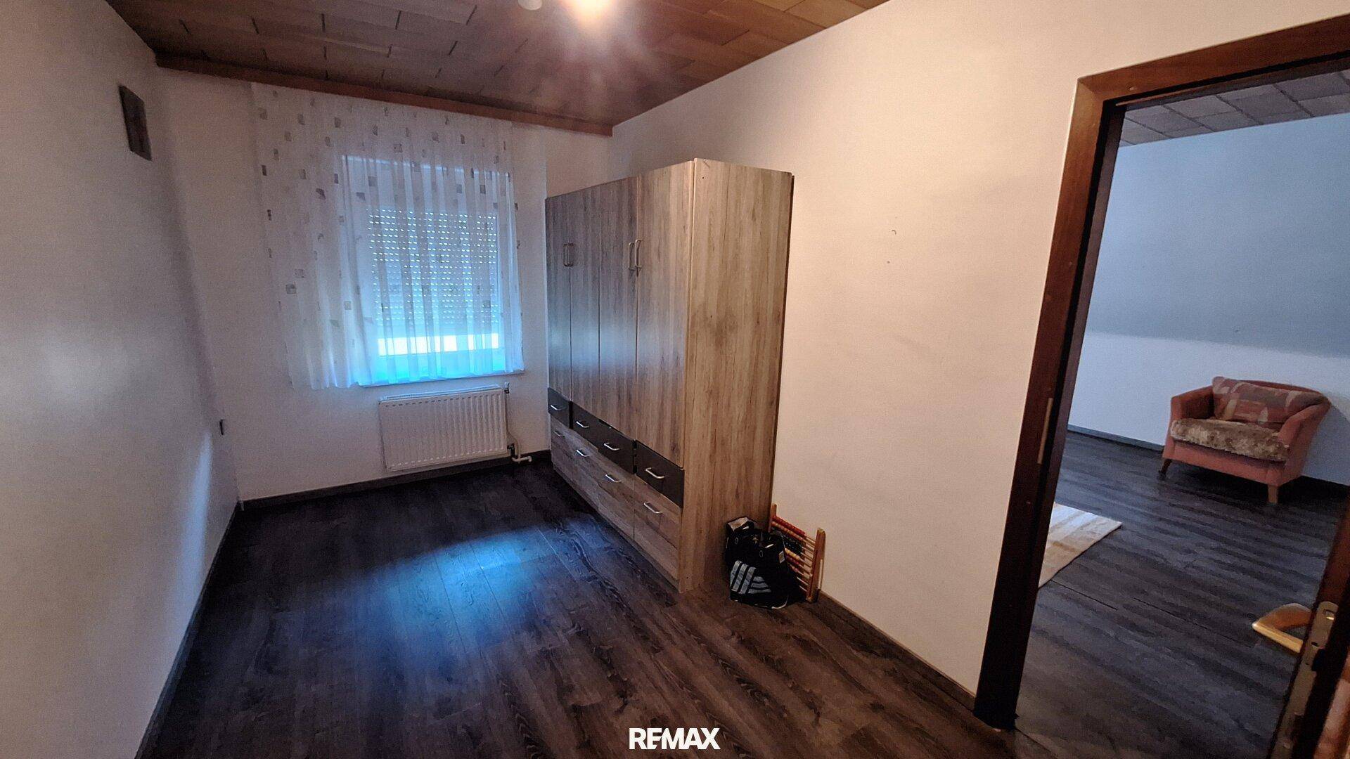 Schlafzimmer mit dunklem Laminatboden, Kleiderschrank und Fenster mit Rollladen.