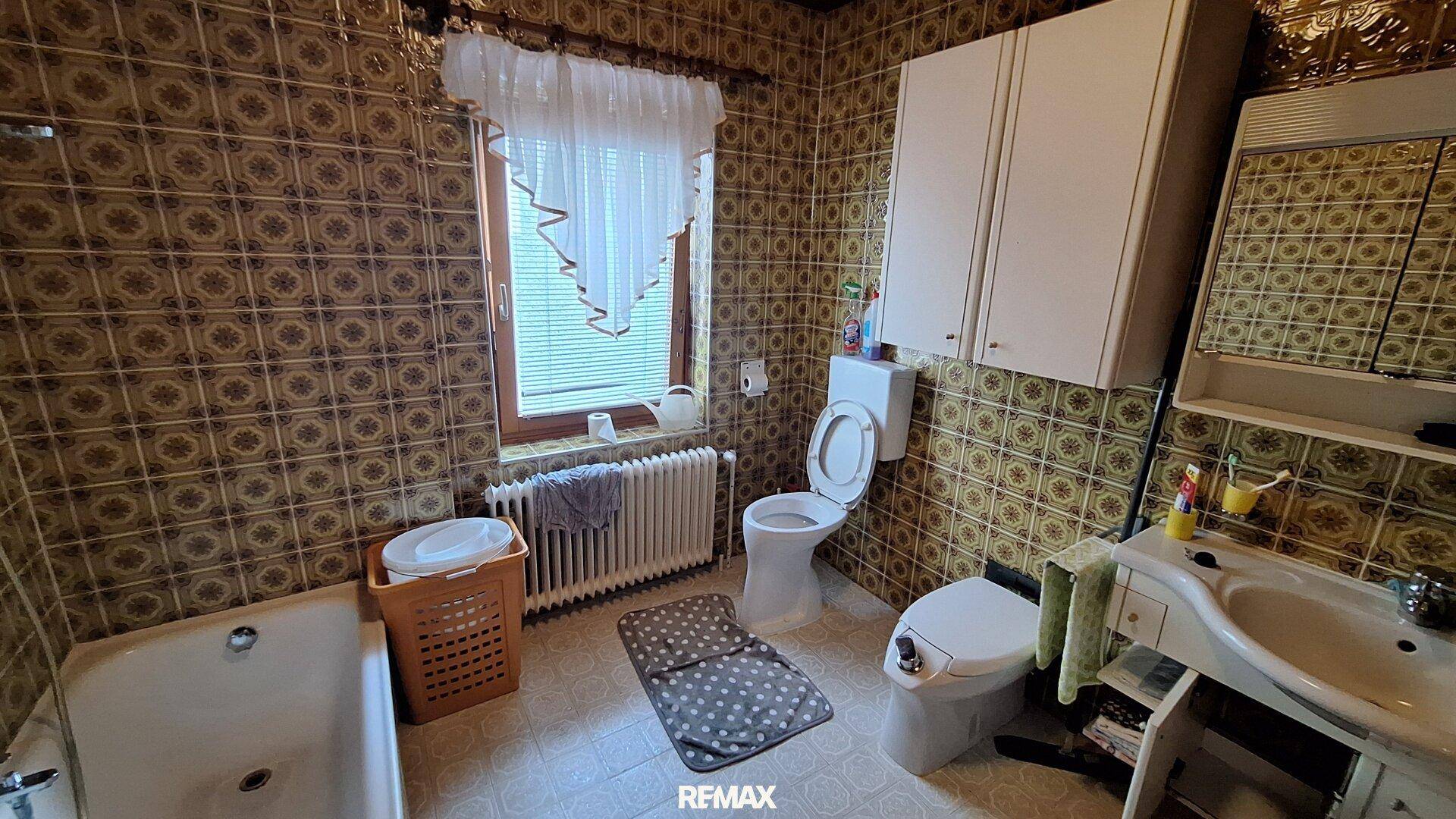 Badezimmer im 80er-Jahre-Stil mit gemusterten Fliesen, Badewanne und Fenster.
