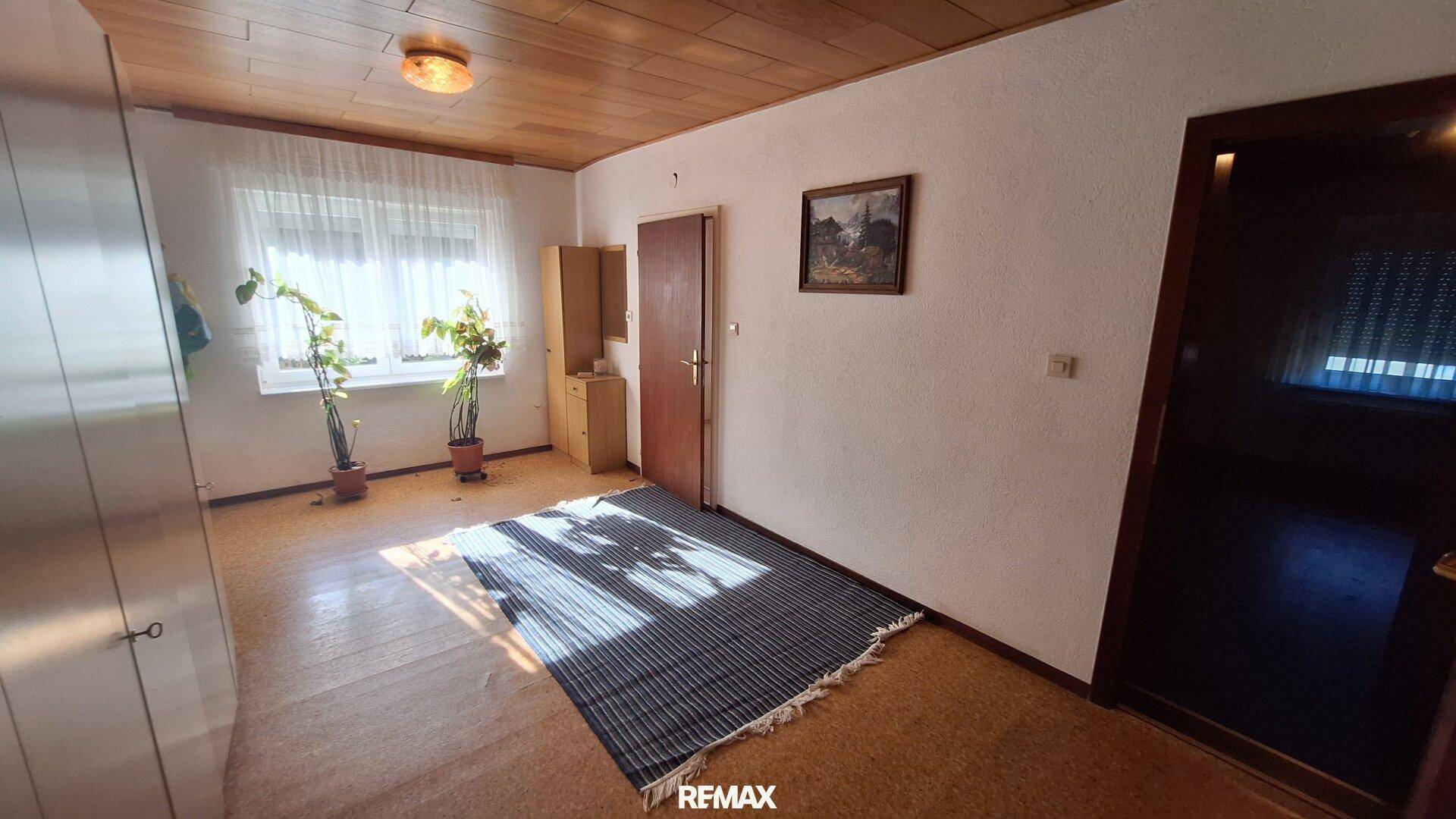 Helles Schlafzimmer mit Korkboden, Holzbalkendecke und einem großen Fenster.