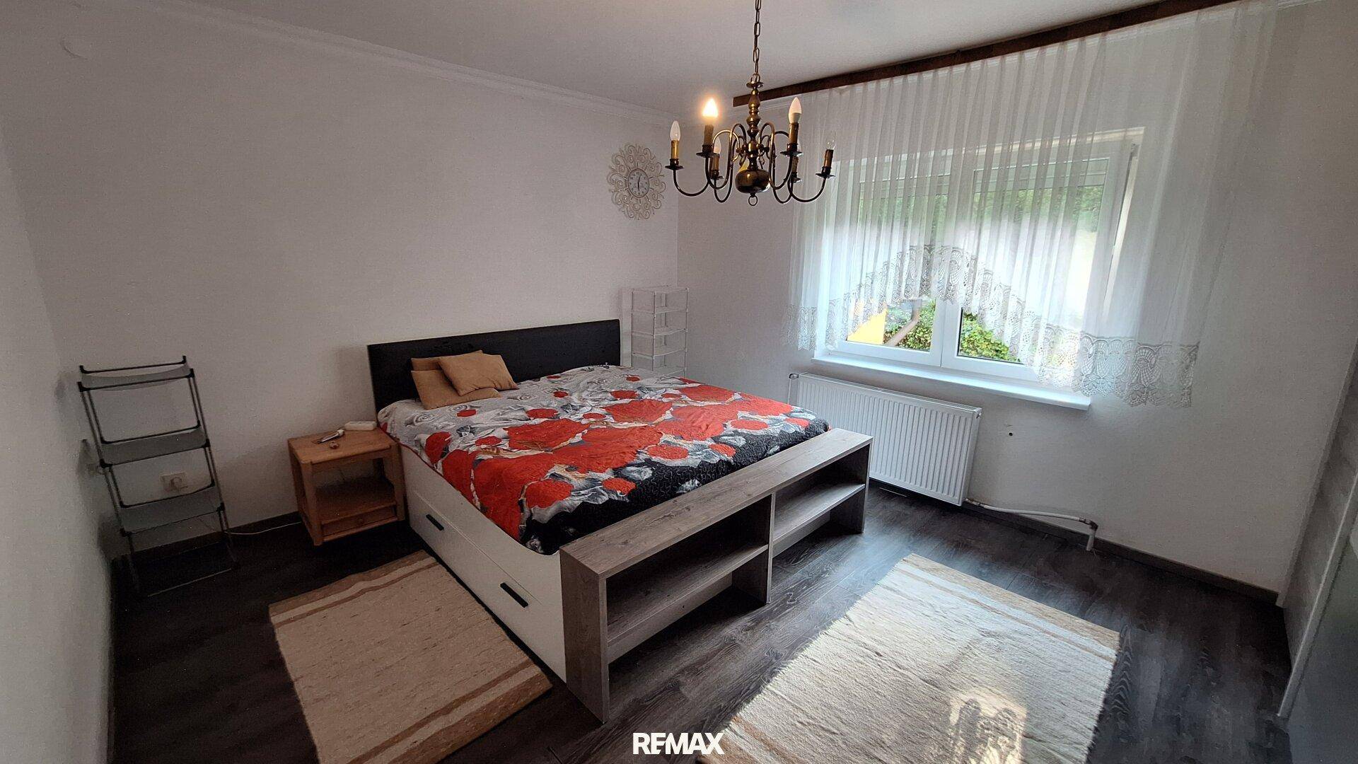Schlafzimmer mit dunklem Laminatboden, Doppelbett und einem Kronleuchter.