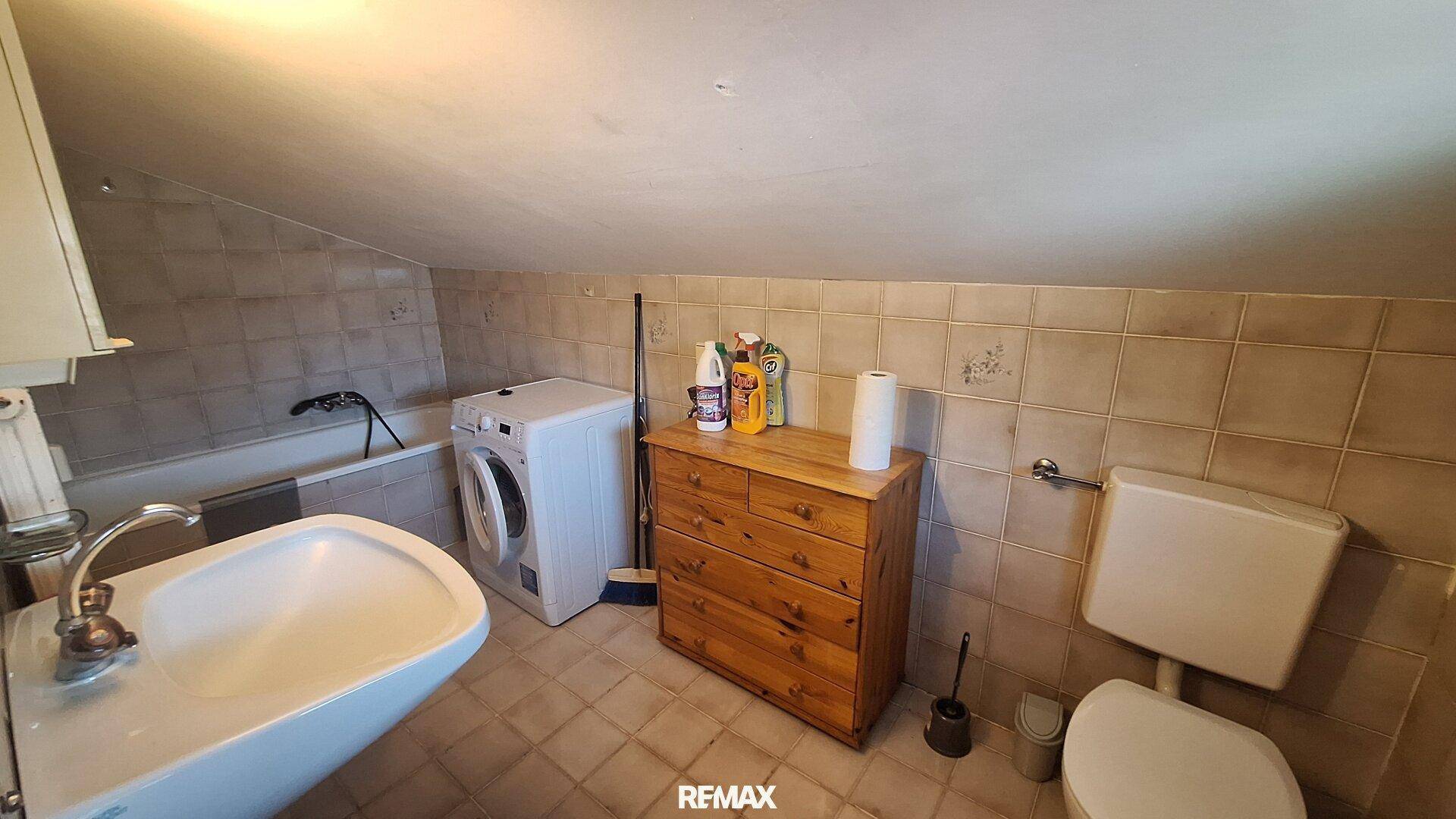Badezimmer im Dachgeschoss mit Badewanne, Waschmaschine und schrägen Wänden.